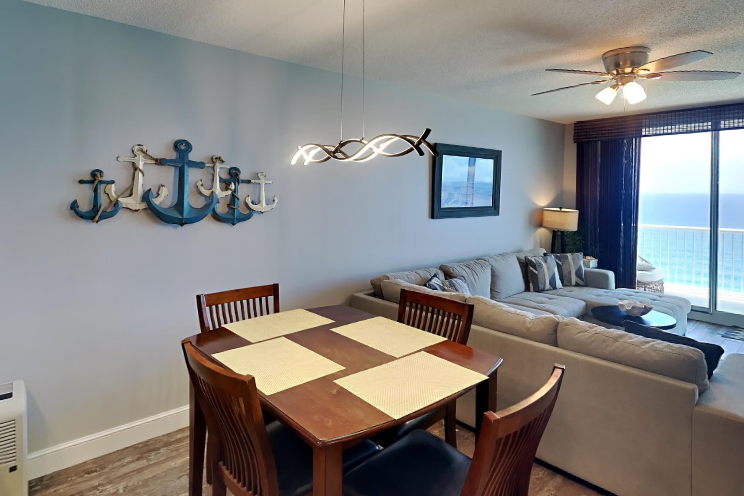A modern living room with a dining area, a ceiling fan, and a view of the ocean.