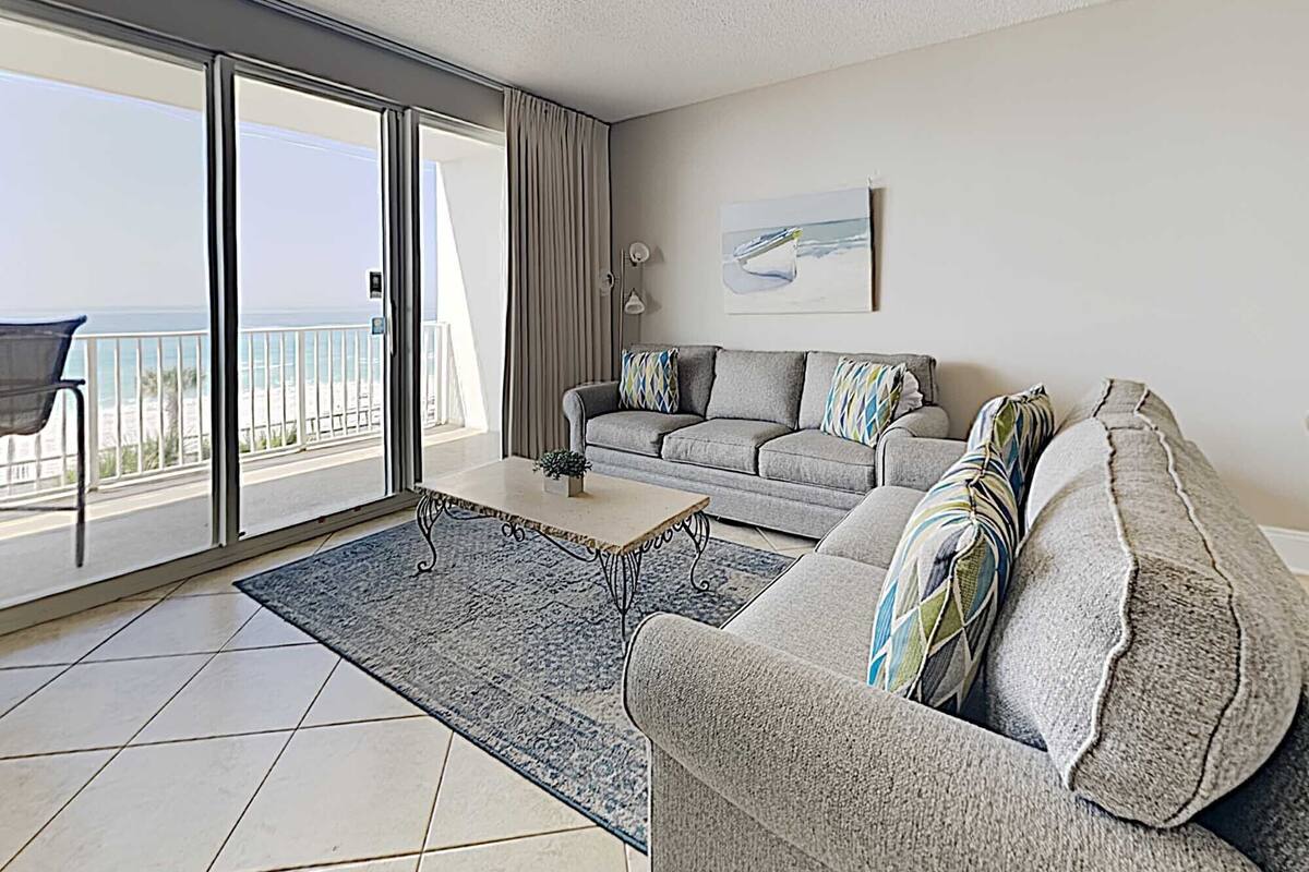 A modern living room with a grey sofa, a coffee table, and a view of the ocean through large sliding doors.