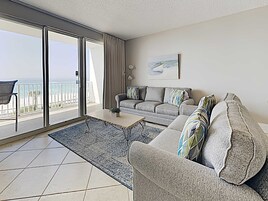 Una sala moderna con un sofá gris, una mesa de centro y vista al océano a través de amplias puertas correderas.