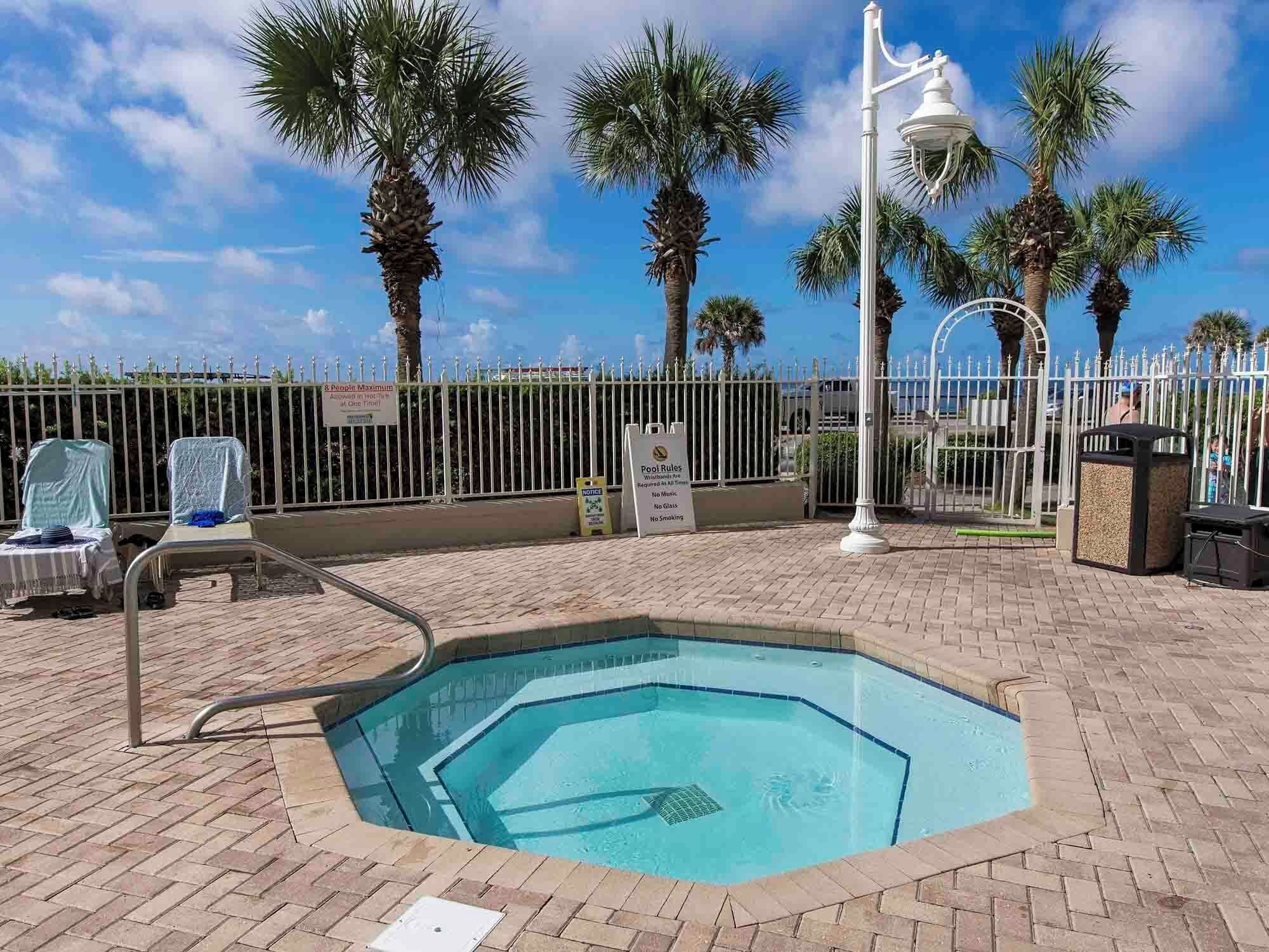 A small octagonal pool with a metal ladder, surrounded by palm trees and a white fence.