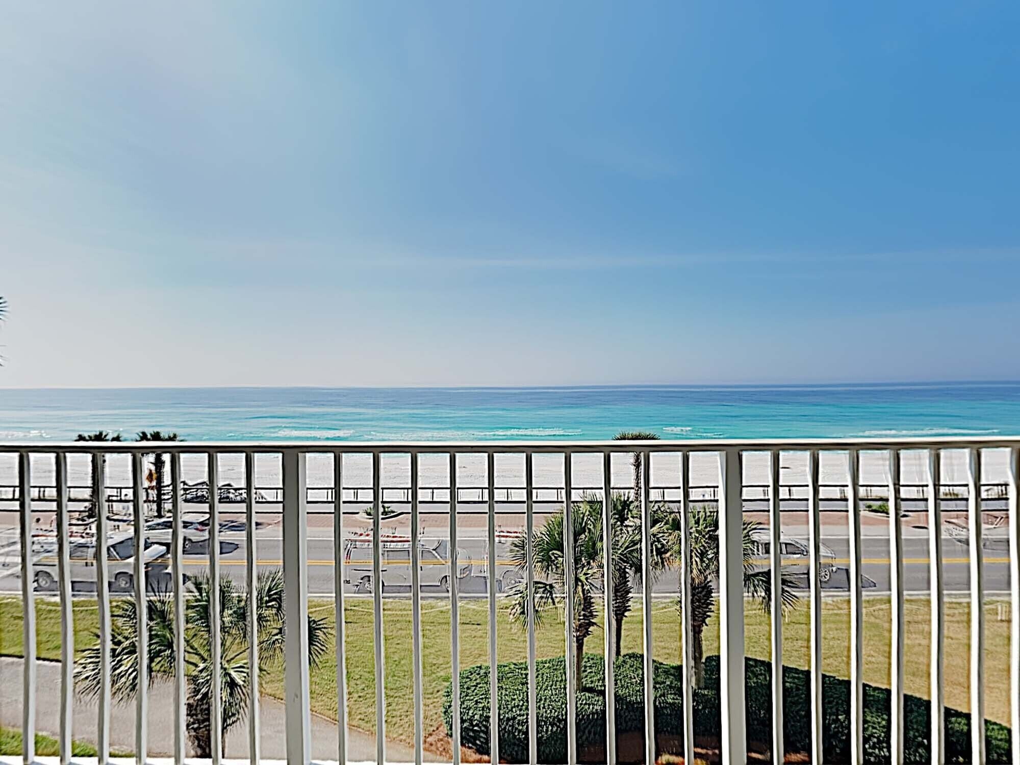 Vista desde un balcón sobre una playa, con cielo despejado.