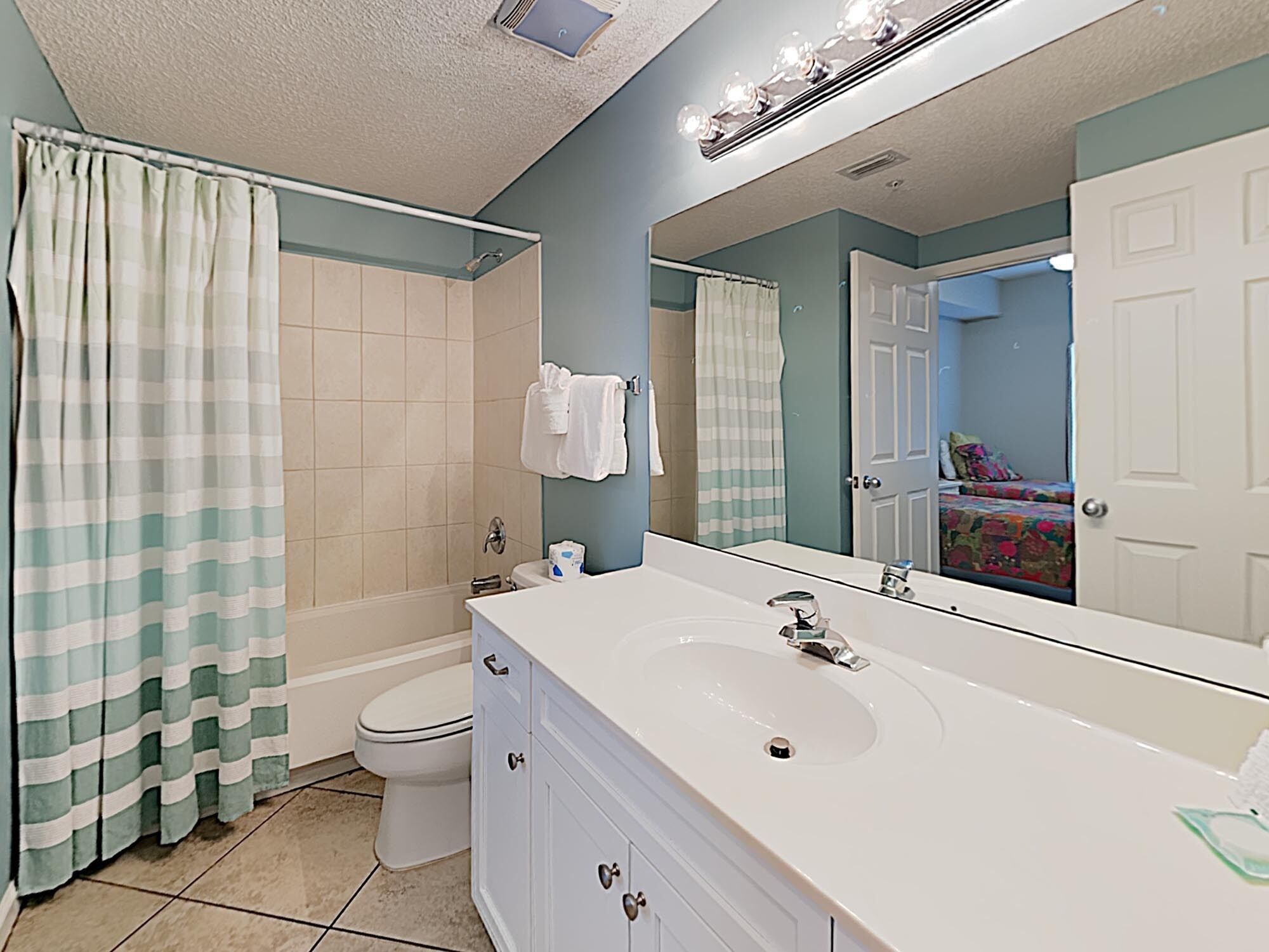 A bathroom with a white sink, a mirror, a shower curtain, and a toilet.