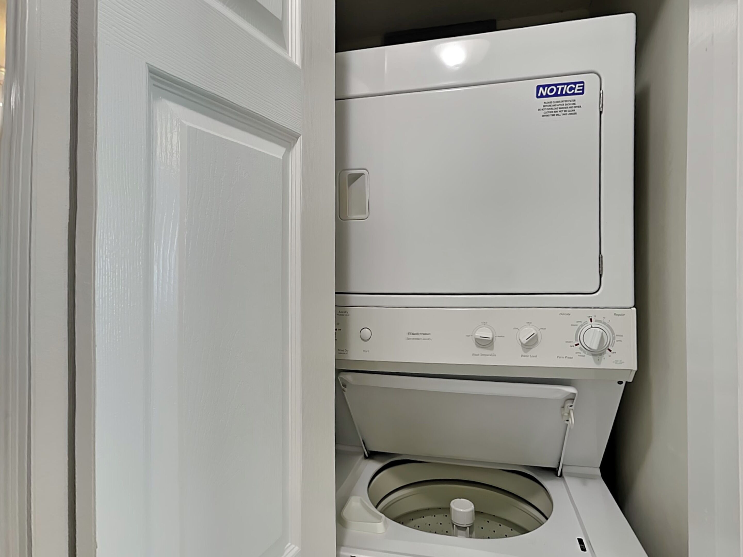 A stacked washer and dryer unit with a notice label on the top.