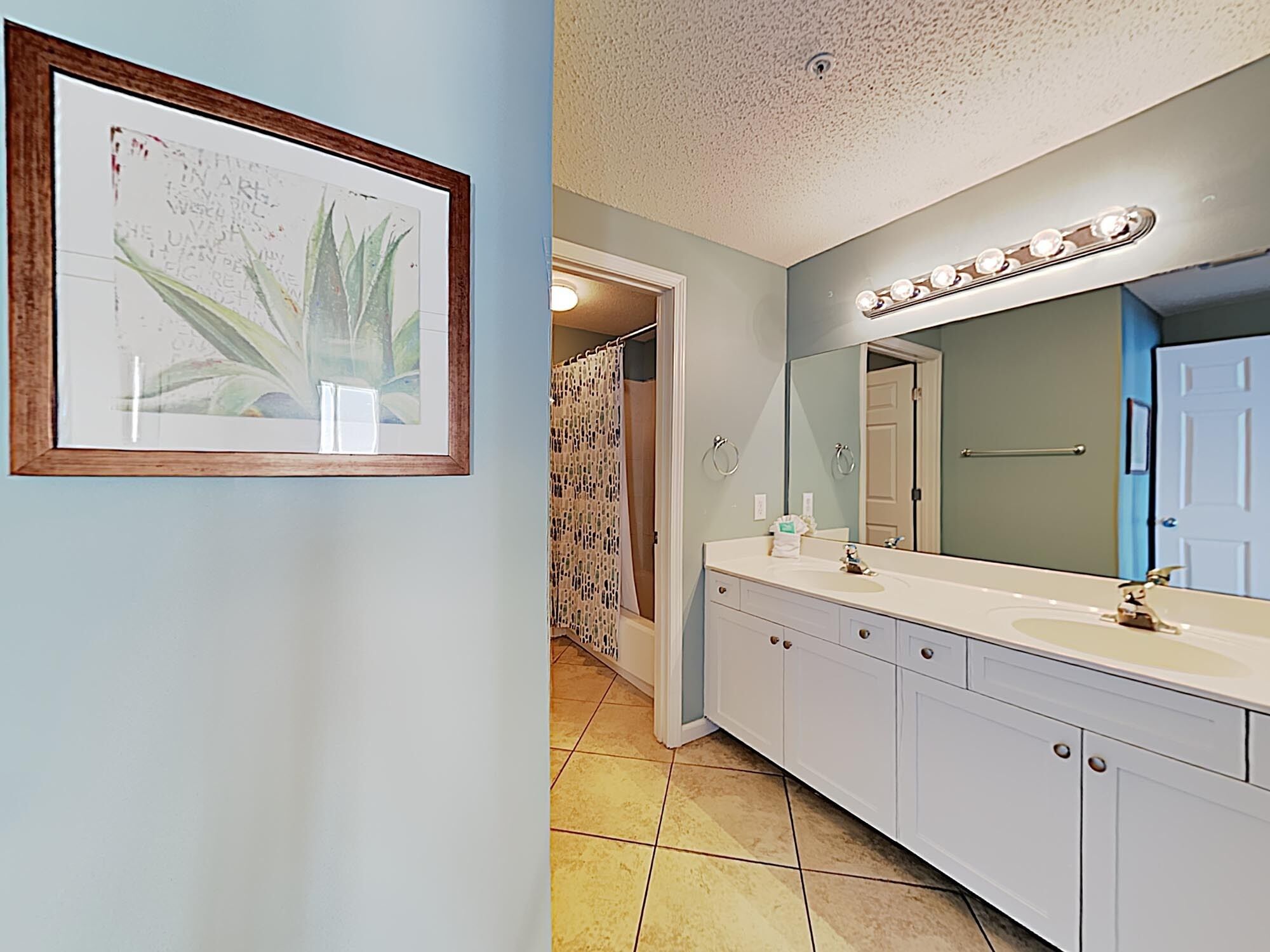 A bathroom with a large mirror, a sink, and a framed botanical print on the wall.