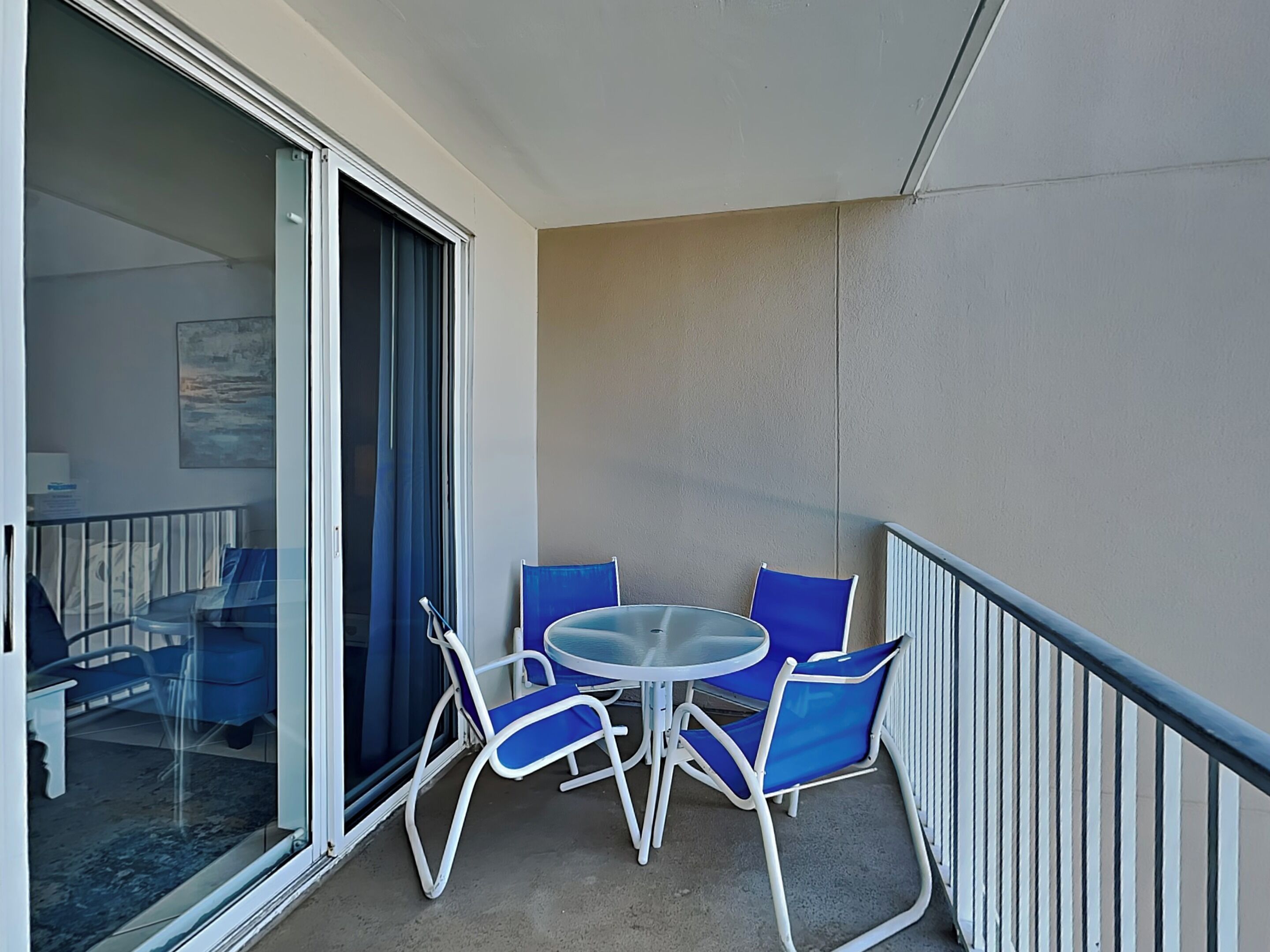 Ein Balkon mit Glastür, einem kleinen runden Tisch und blauen Stühlen.