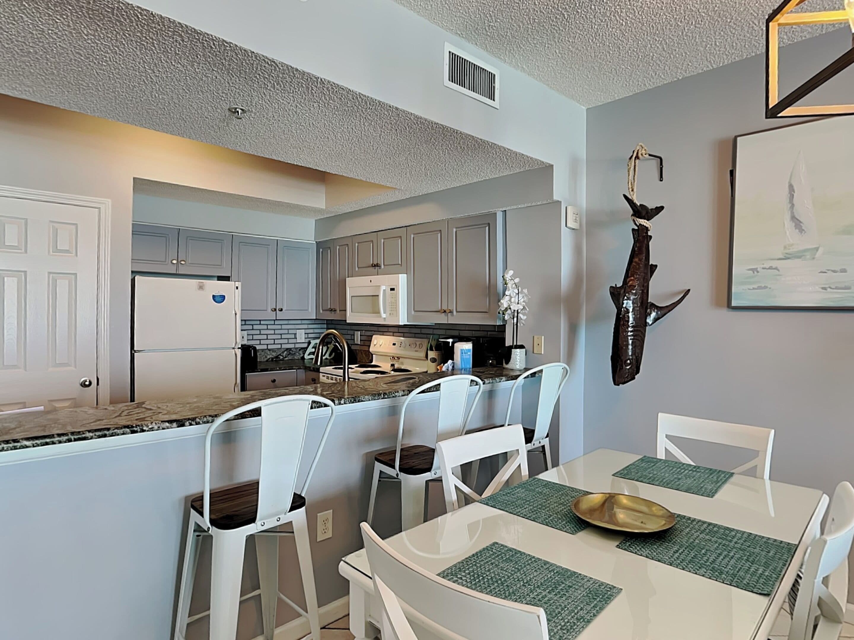 A modern kitchen with white cabinets, a microwave, and a stove. There is a dining area with a white table and chairs, and a decorative fish on the wall.