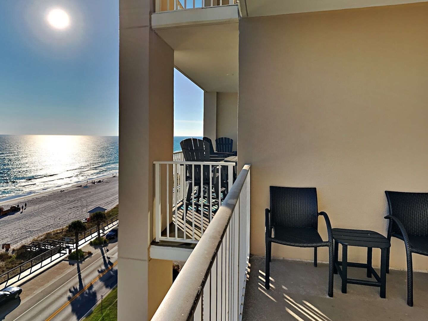 A balcony with a view of the beach and ocean, featuring two chairs and a table.