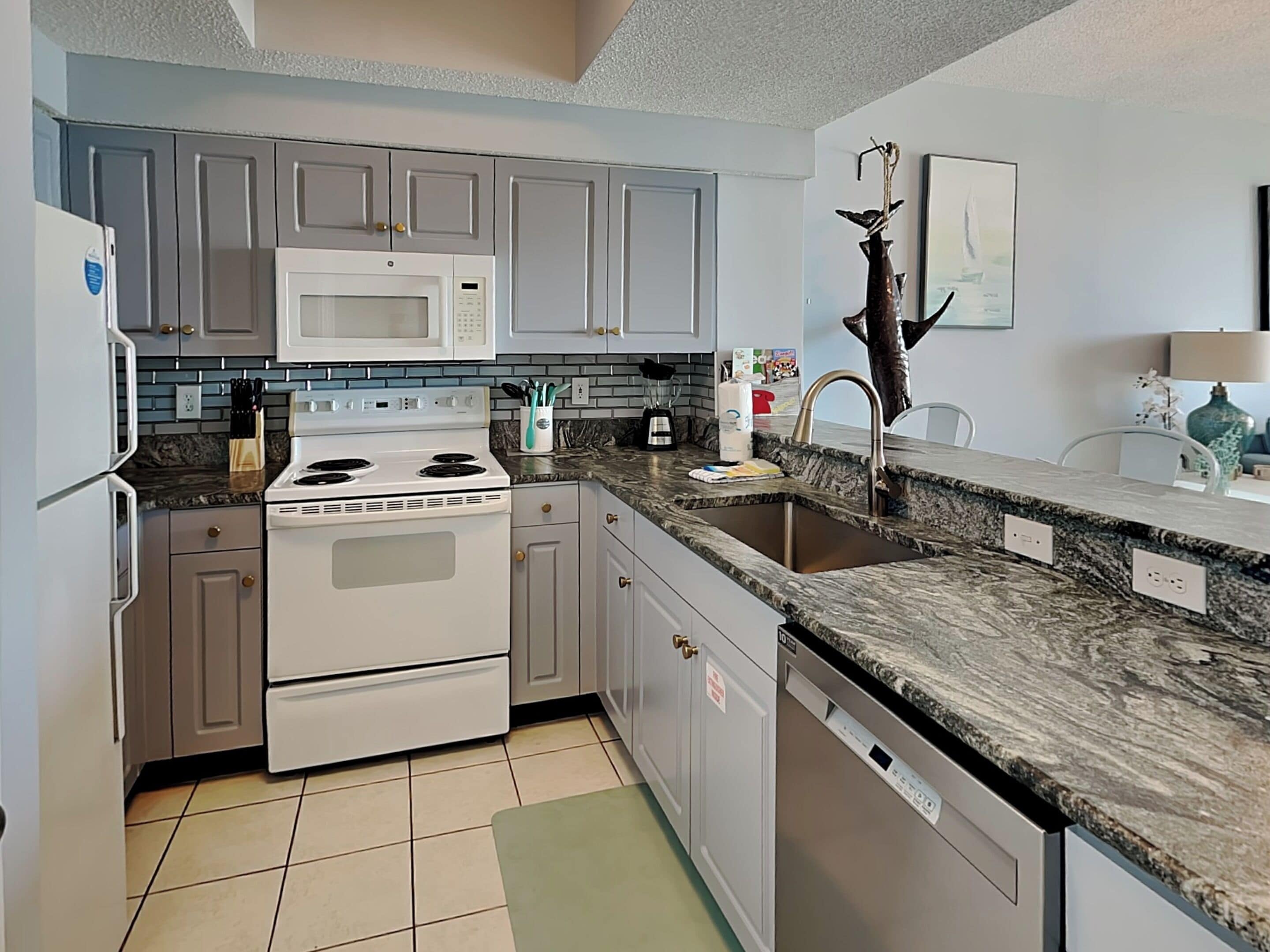 A modern kitchen with grey cabinets, a white stove, a microwave, and a granite countertop.