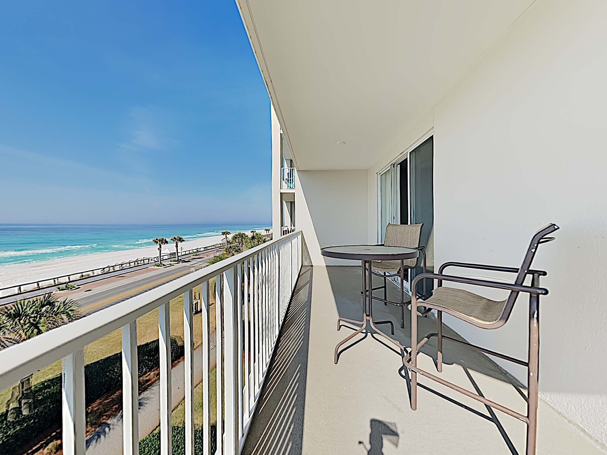 A balcony with a table and chairs overlooking a beach.