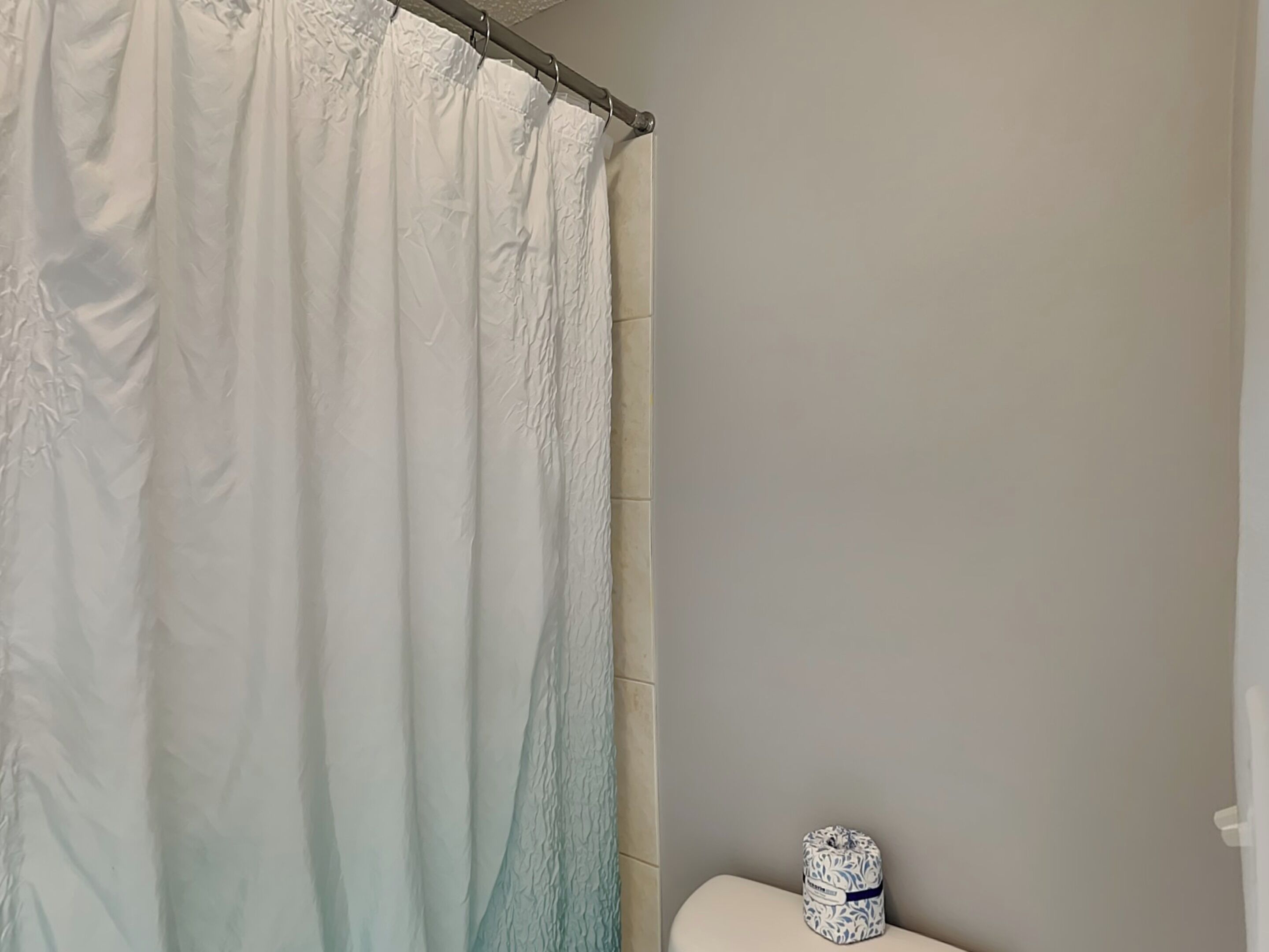 A bathroom with a white shower curtain, a toilet, and a small decorative item on the toilet.