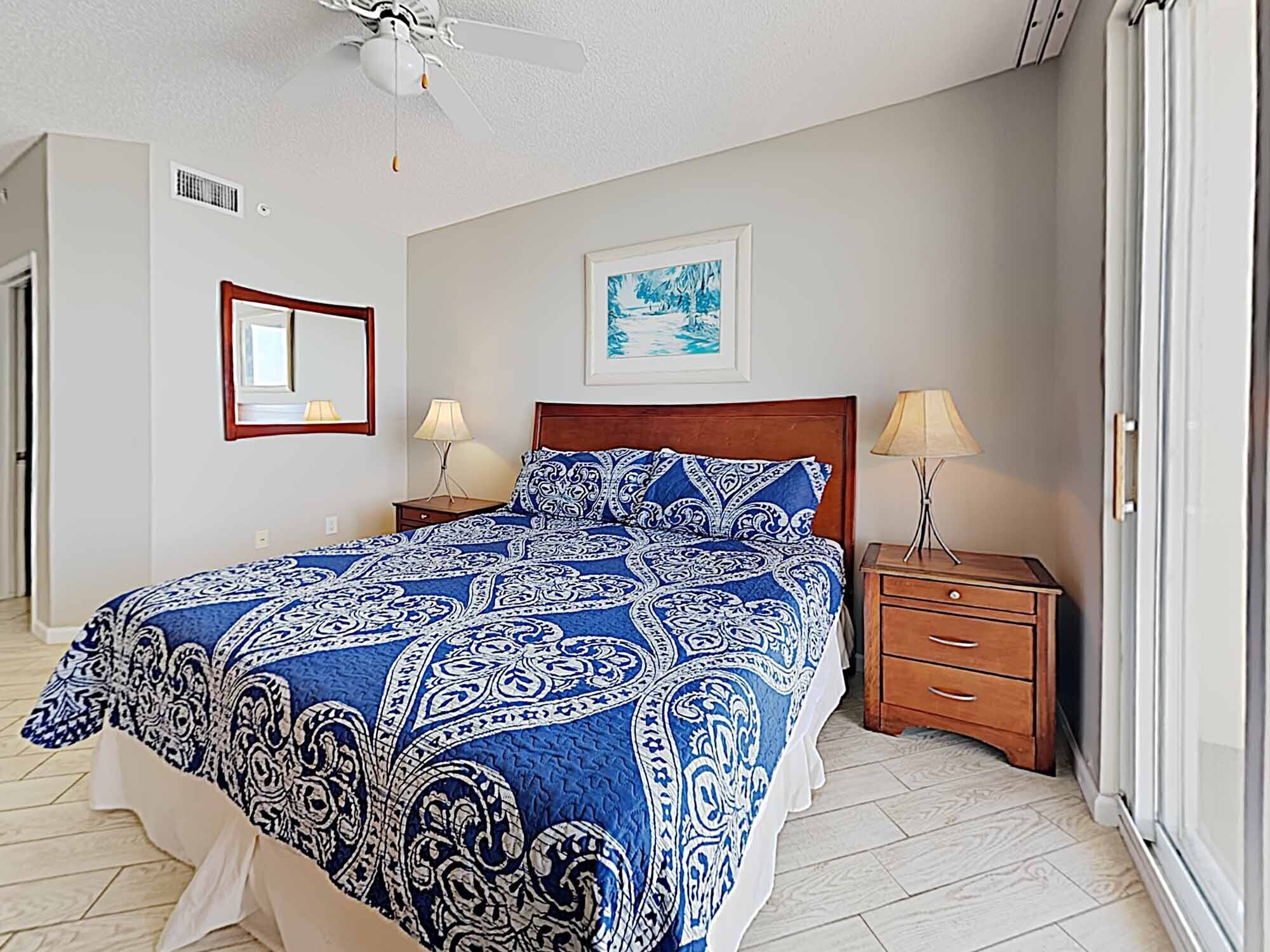 A bedroom with a bed, two bedside tables, a ceiling fan, a mirror, and a framed picture on the wall.