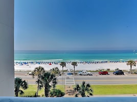 Une plage avec des parasols et des palmiers, une route avec des voitures et un ciel bleu dégagé.