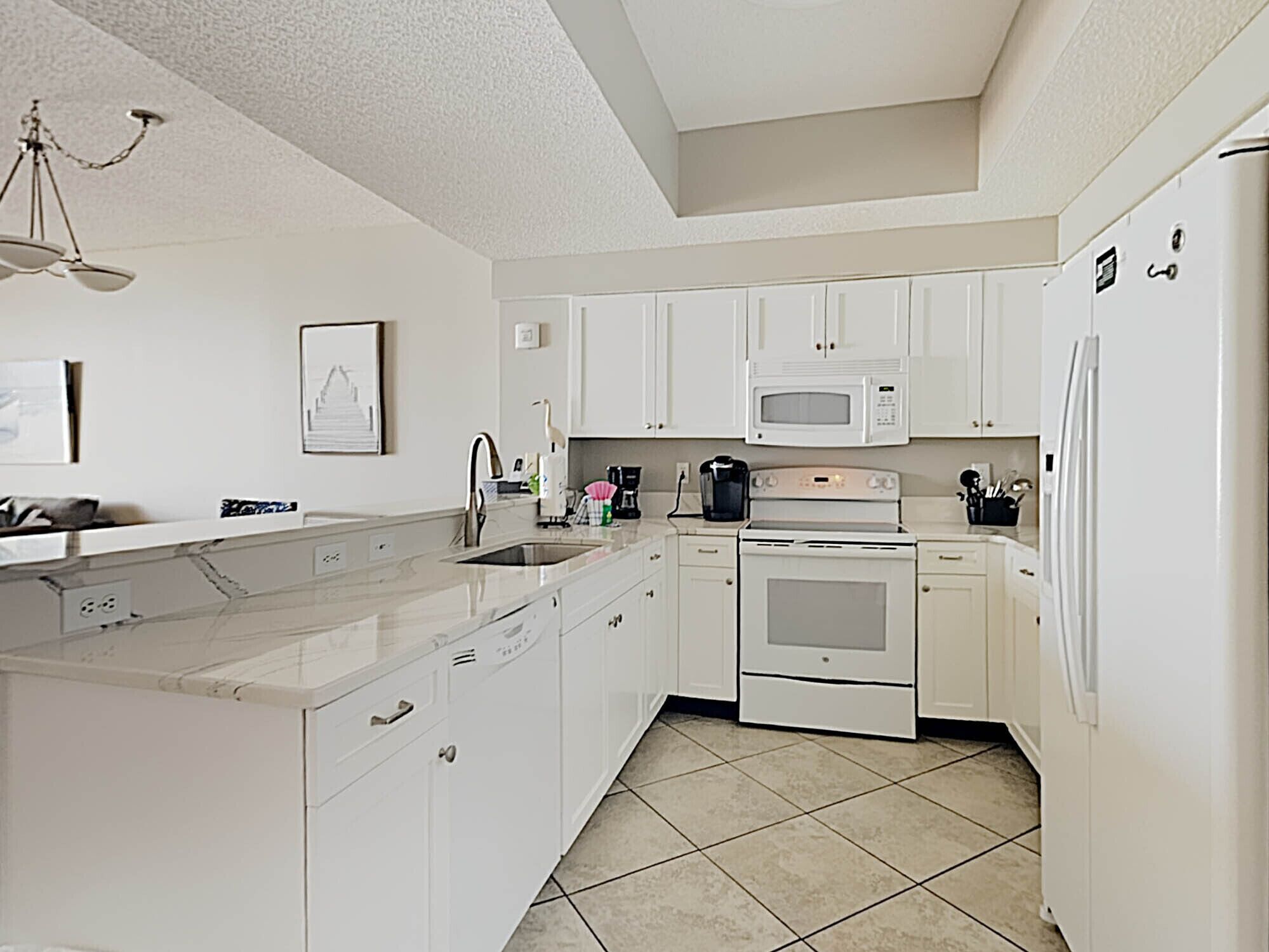 A modern kitchen with white cabinets, a stainless steel sink, a microwave, and a stove.
