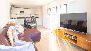 A modern living room with a sofa, a TV, and a wooden entertainment unit. - GRACE SUITE LONDON (London)