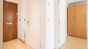 A hallway with wooden flooring, white walls, and a wooden door on the left. - GRACE SUITE LONDON (London)