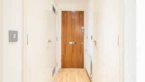 A hallway with a wooden door at the end, white walls, and a light switch on the left. - GRACE SUITE LONDON (London)