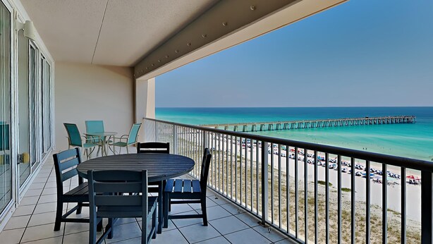 A balcony with a table and chairs, overlooking a beach with a pier.