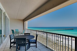 A balcony with a table and chairs, overlooking a beach with a pier.