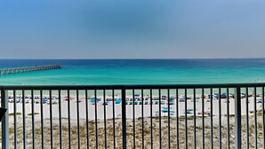 A beach view with a pier extending into the ocean, a sandy beach with umbrellas, and a clear sky.