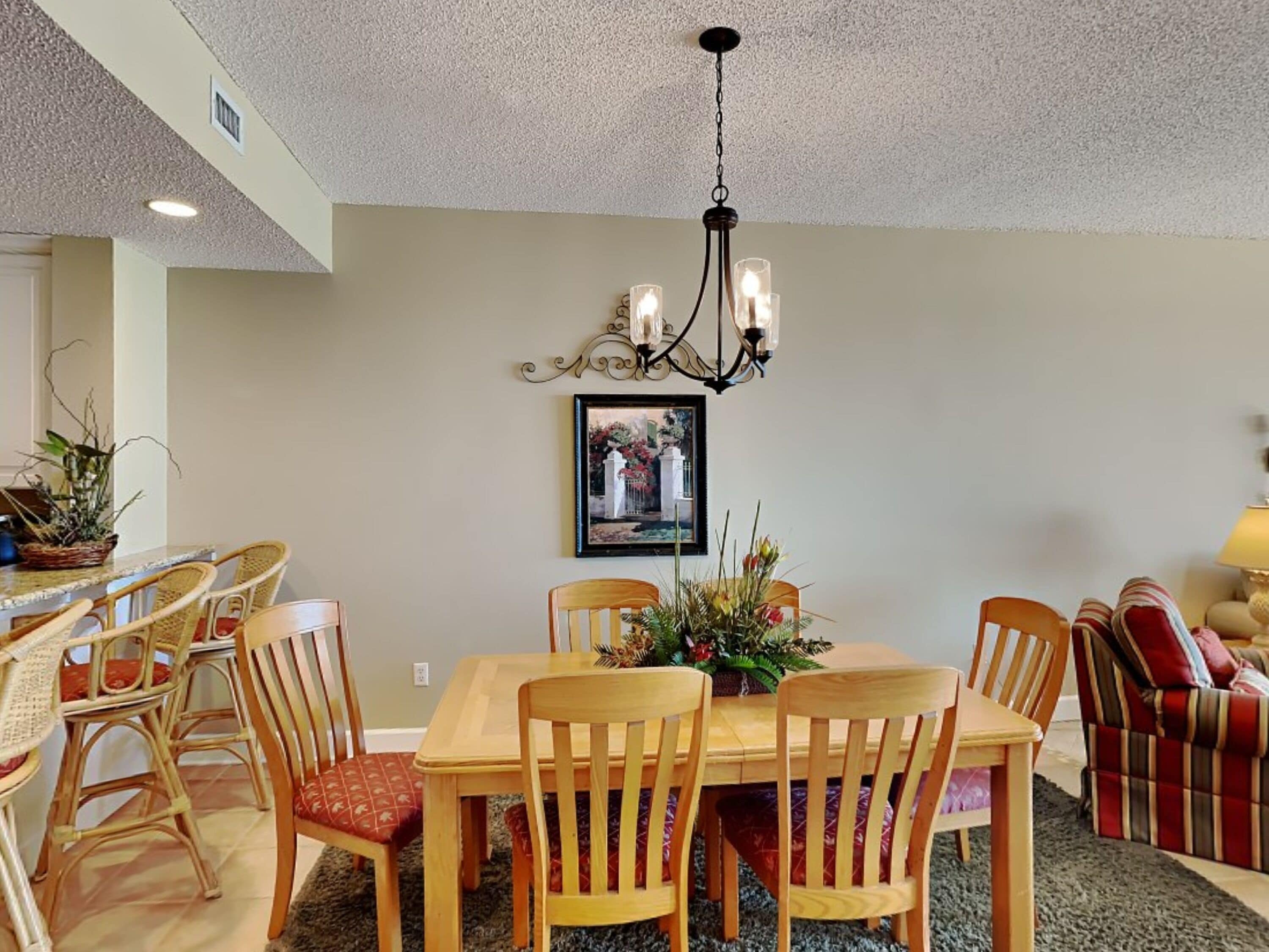 A dining area with a wooden table and chairs, a chandelier, and a framed picture on the wall.