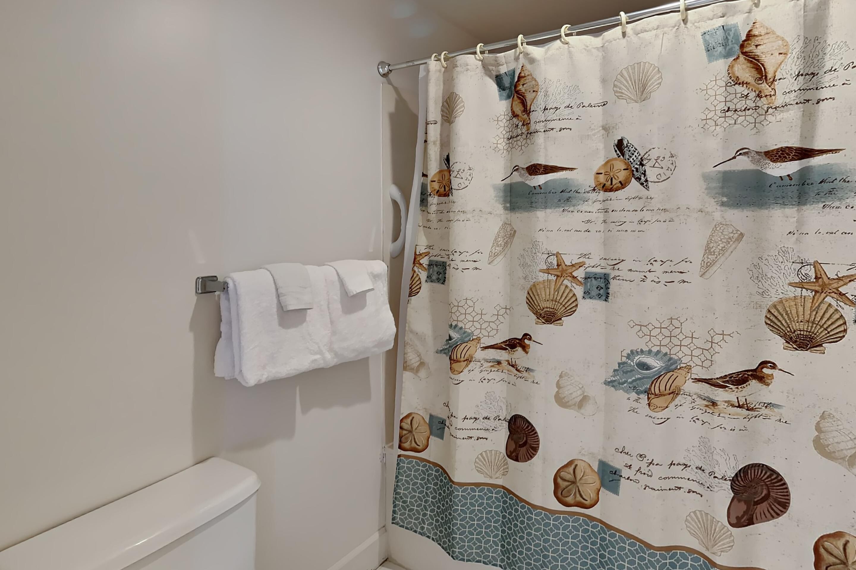 A bathroom with a shower curtain featuring sea shells and birds, a white toilet, and a towel rack with a white towel.