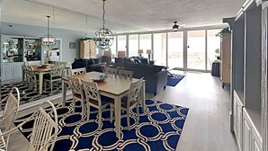A spacious living area with a dining table, sofas, and a large window providing a view of the outdoors.