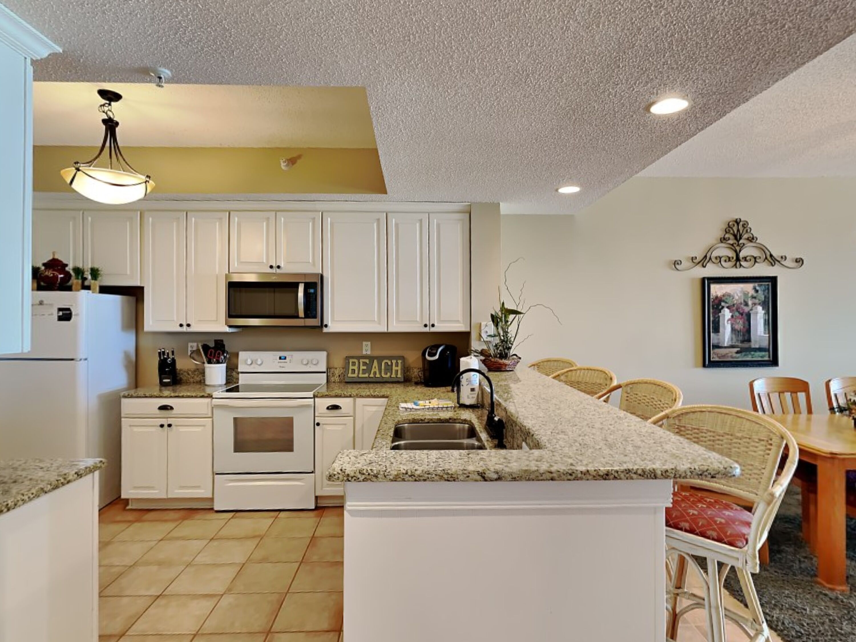 A kitchen with white cabinets, a microwave, an oven, a sink, and a dining area with wicker chairs.