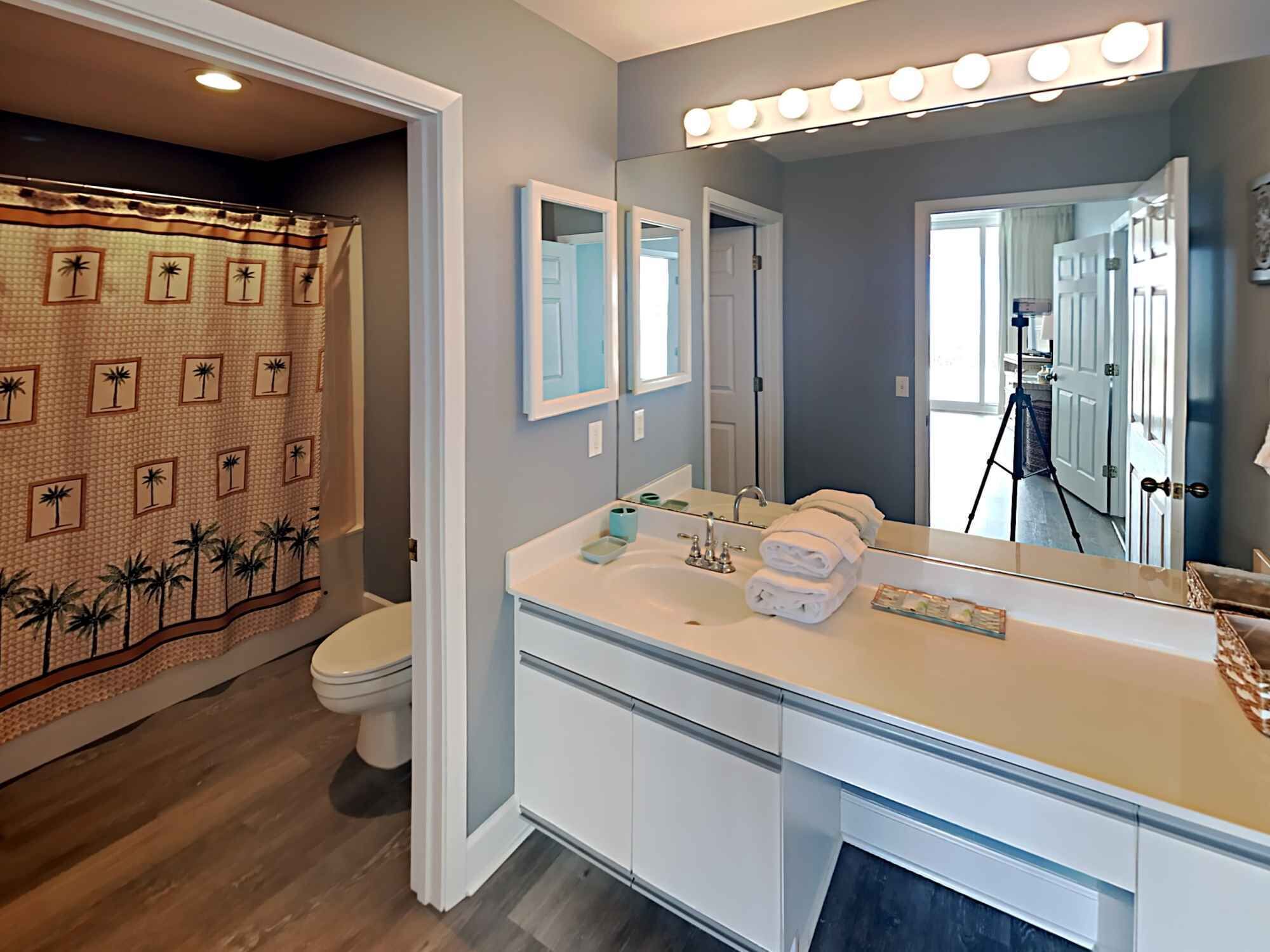 Une salle de bain équipée d’un meuble-lavabo, de toilettes et d’un rideau de douche orné de motifs de palmiers.