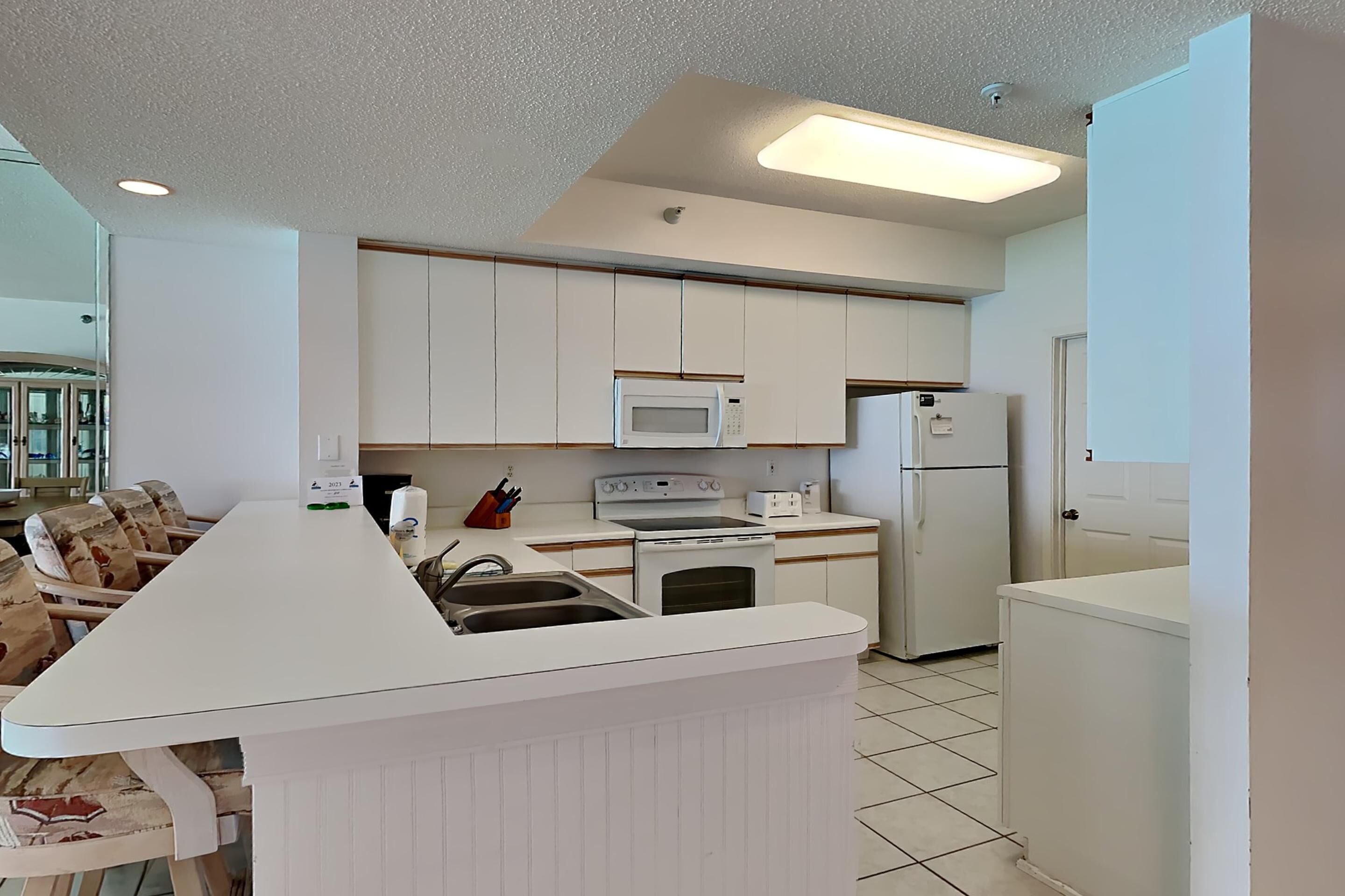 Eine moderne Küche mit weißen Schränken, einer zentralen Kochinsel mit Spüle, Mikrowelle, Backofen und Kühlschrank.