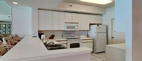 Eine moderne Küche mit weißen Schränken, einer zentralen Kochinsel mit Spüle, Mikrowelle, Backofen und Kühlschrank.