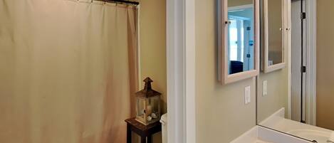 A bathroom with a shower curtain, a toilet, a small table with a lantern, and a mirror with a cabinet above it.