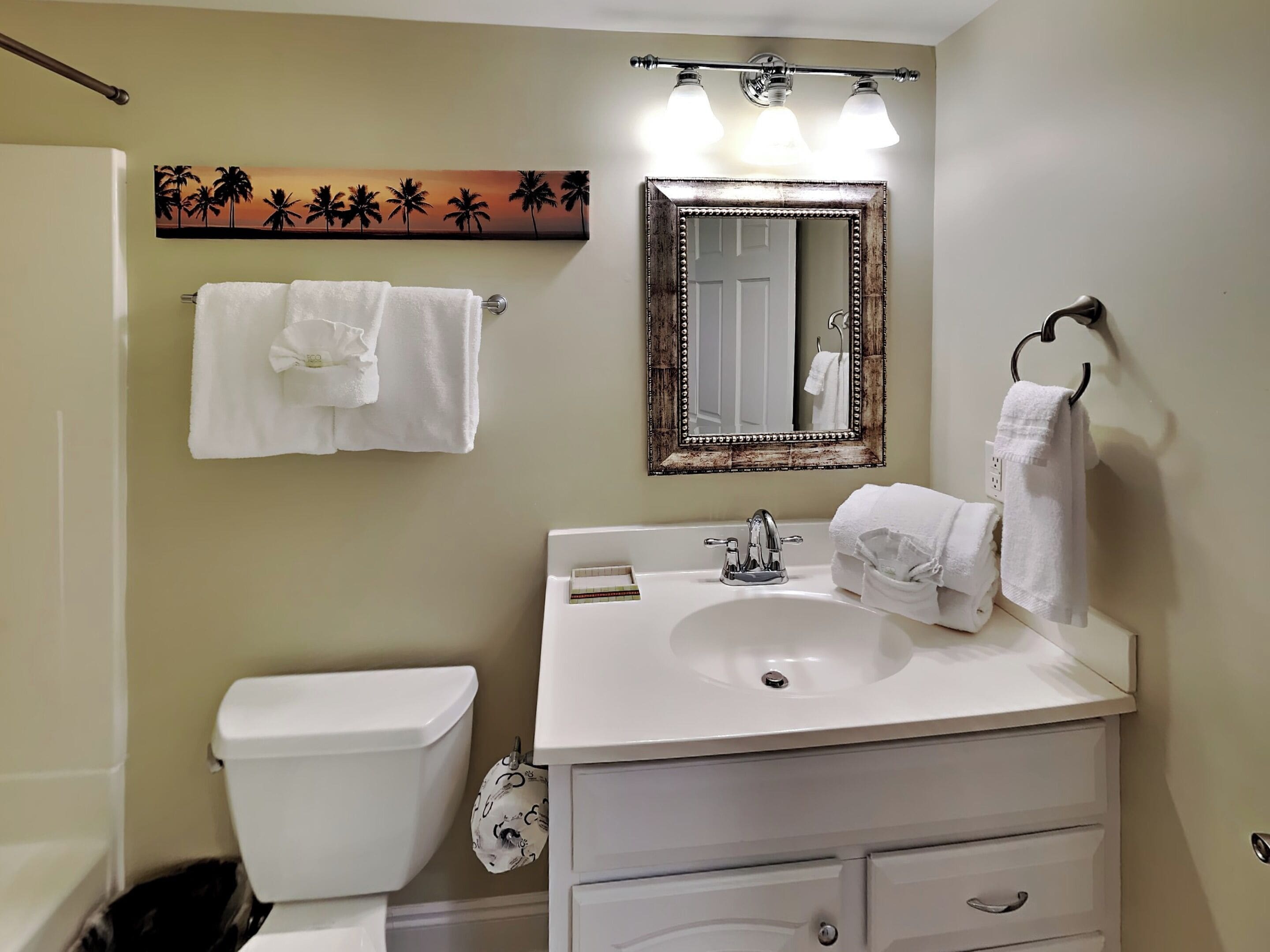 Um banheiro com pia branca, um espelho com moldura decorativa e um porta-toalhas com duas toalhas.