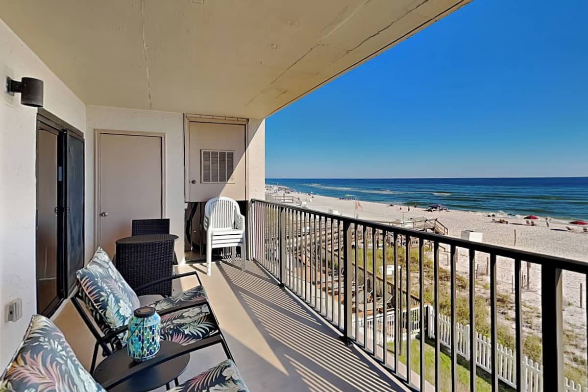 Ein Balkon mit Blick auf den Strand, eine Tür, ein Stuhl und ein Tisch mit einem dekorativen Gegenstand.