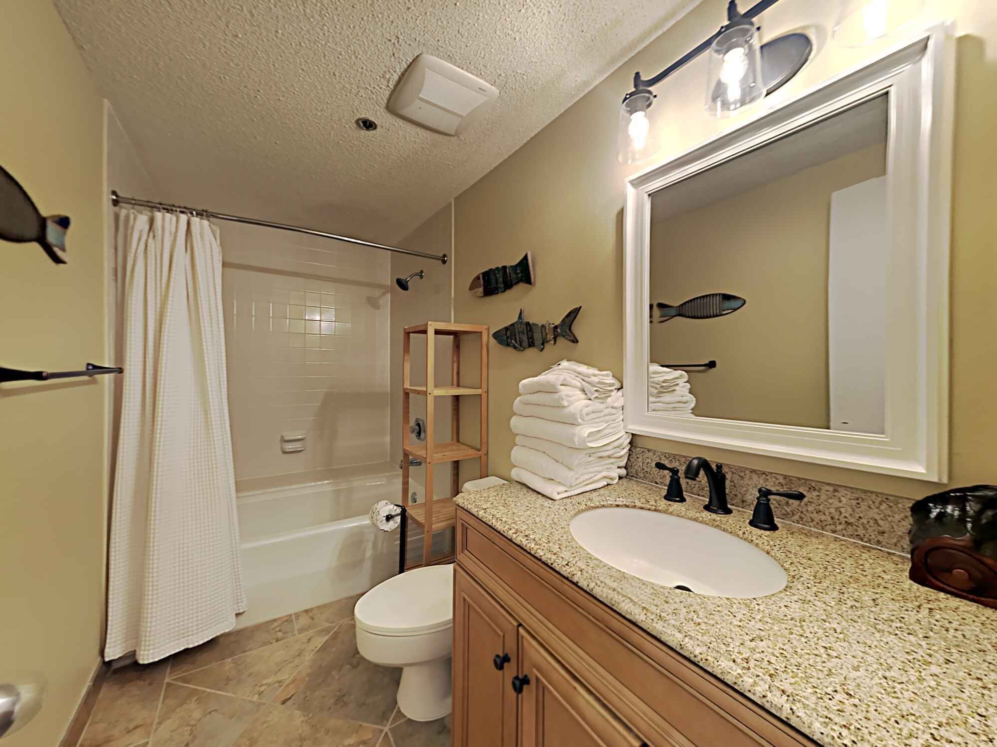 A bathroom with a shower, toilet, sink, and a mirror with fish decorations.