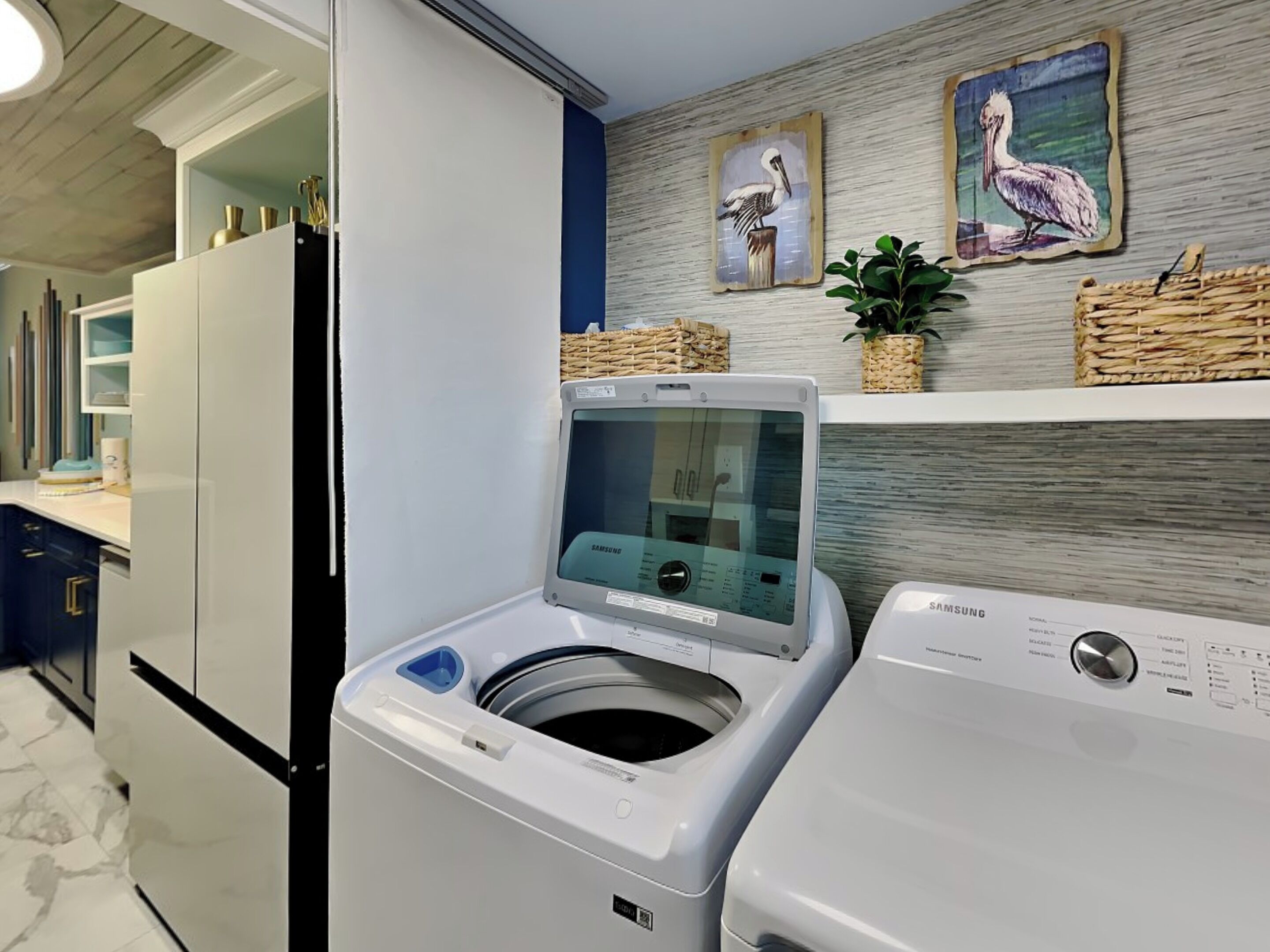 A laundry room with a front-loading washer and dryer, a wall-mounted shelf with decorative items, and a refrigerator.