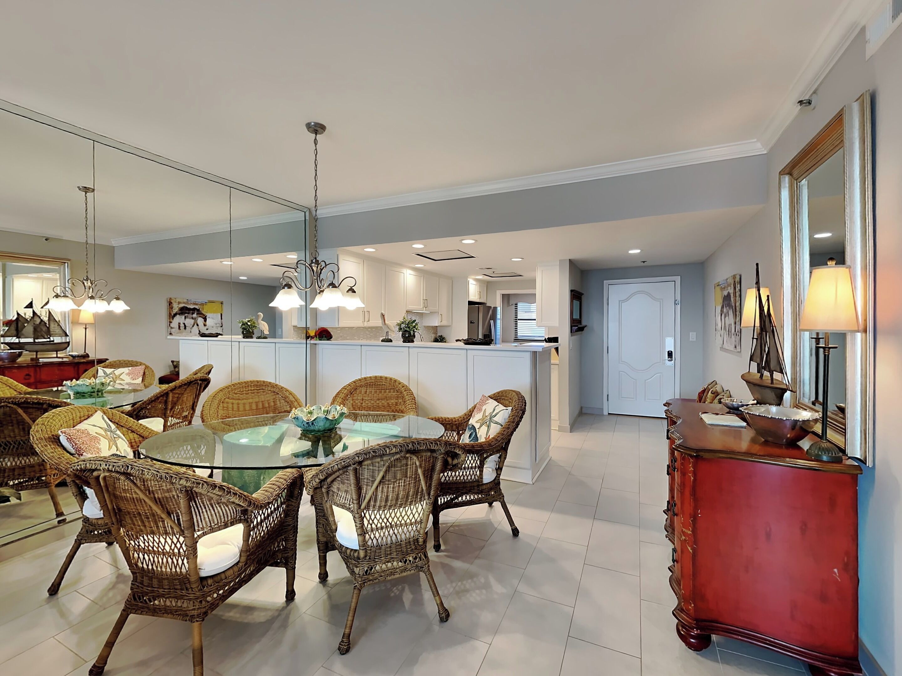 A modern kitchen with white cabinets, a central island, and a dining area with wicker chairs and a glass table.