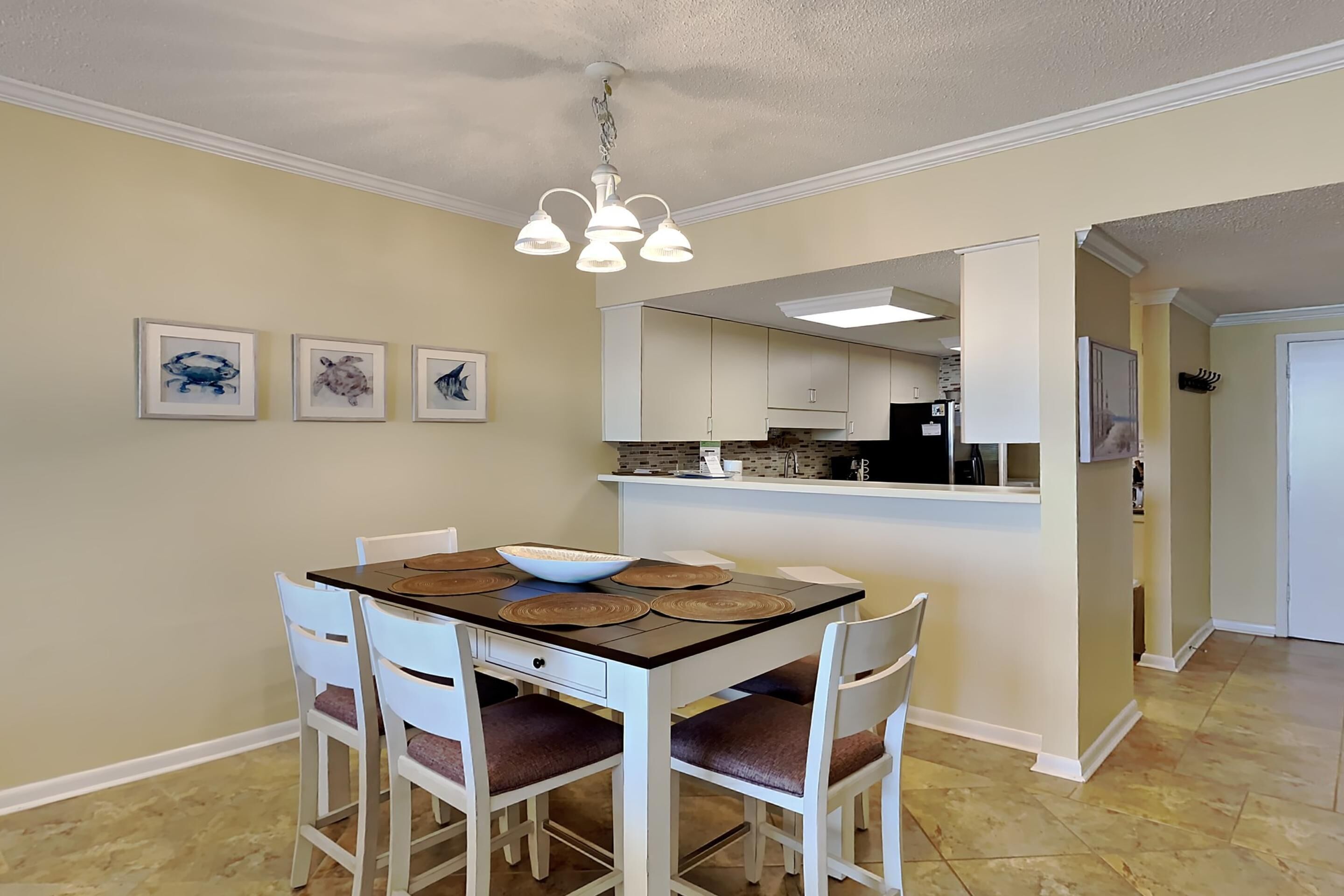 A dining area with a table, chairs, and a chandelier. There are framed pictures on the wall.