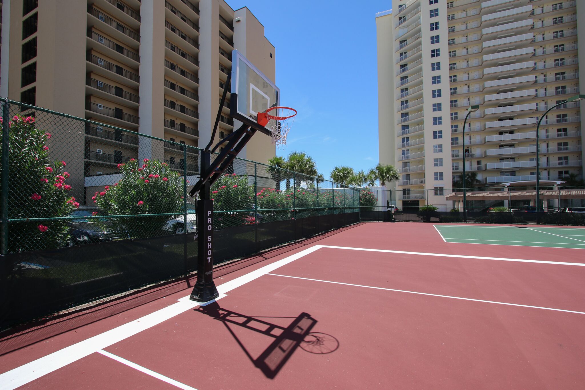 A basketball court with a net, surrounded by a fence and tall buildings.