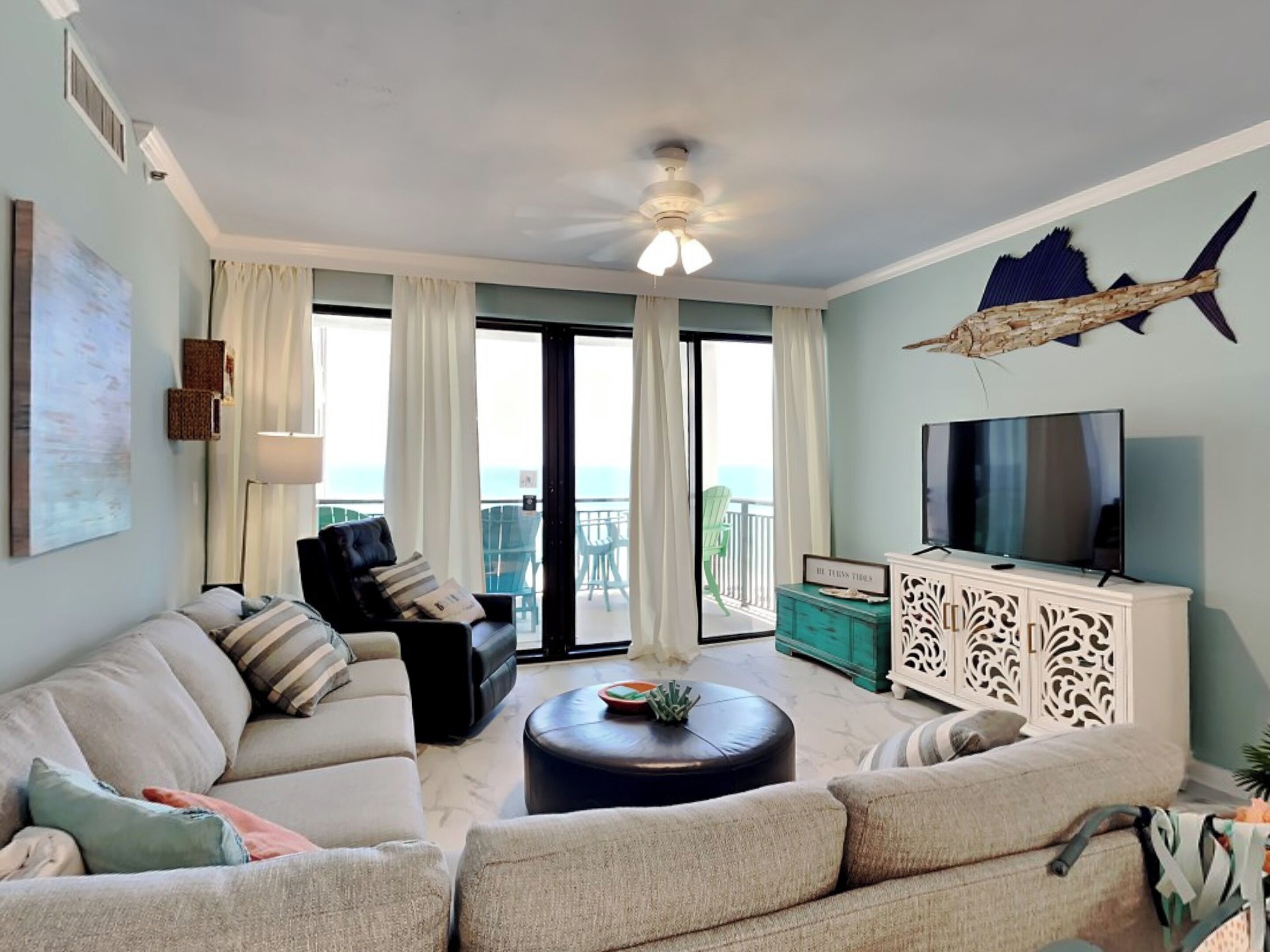 A living room with a sofa, a coffee table, a TV, and a balcony with a view.