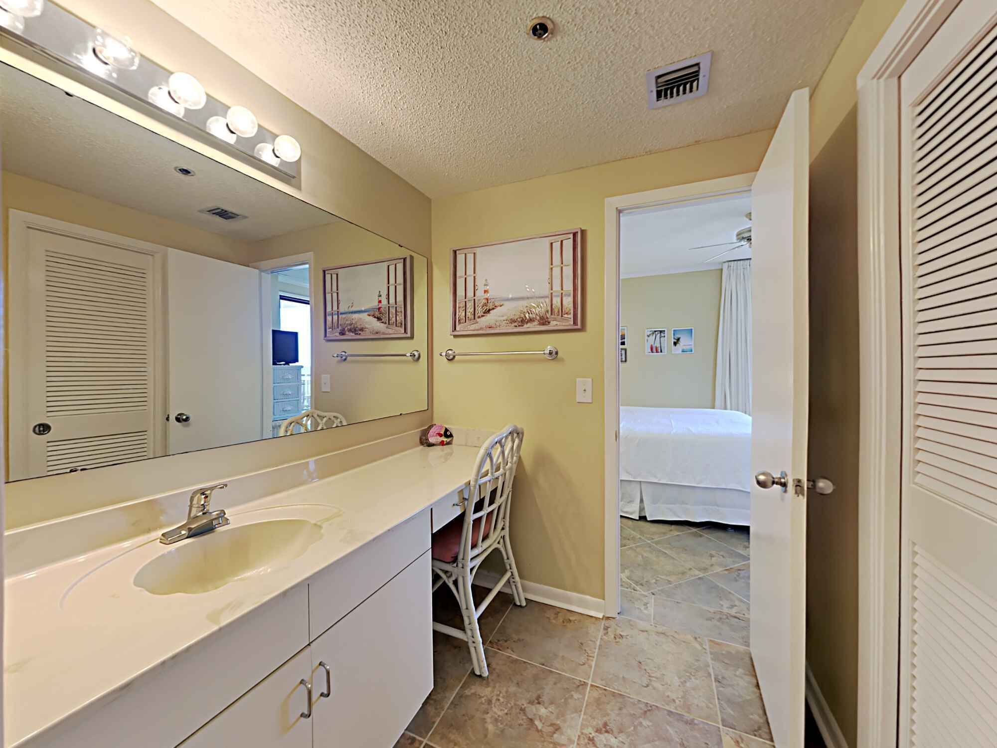A bathroom with a large mirror, vanity with a sink, towel rack, and a chair.