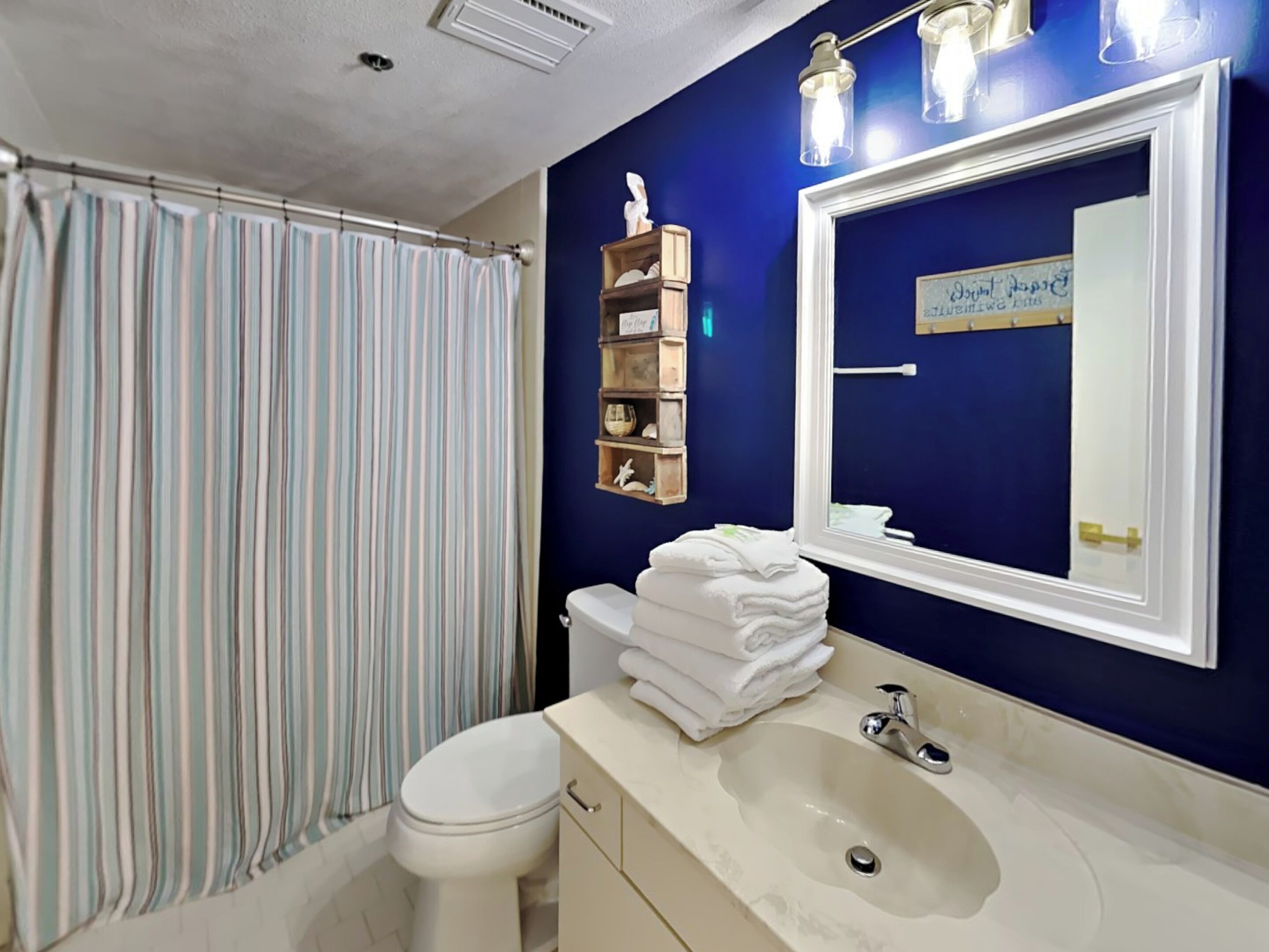 Une salle de bain avec un rideau de douche à rayures, des toilettes blanches, un lavabo avec un miroir et une étagère avec des serviettes.