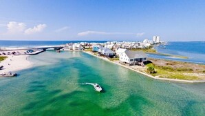 An aerial view of a coastal area with clear turquoise waters, a bridge, and a row of white buildings along the shore. - Muskoka by Southern Vacation Rentals (Gulf Shores)
