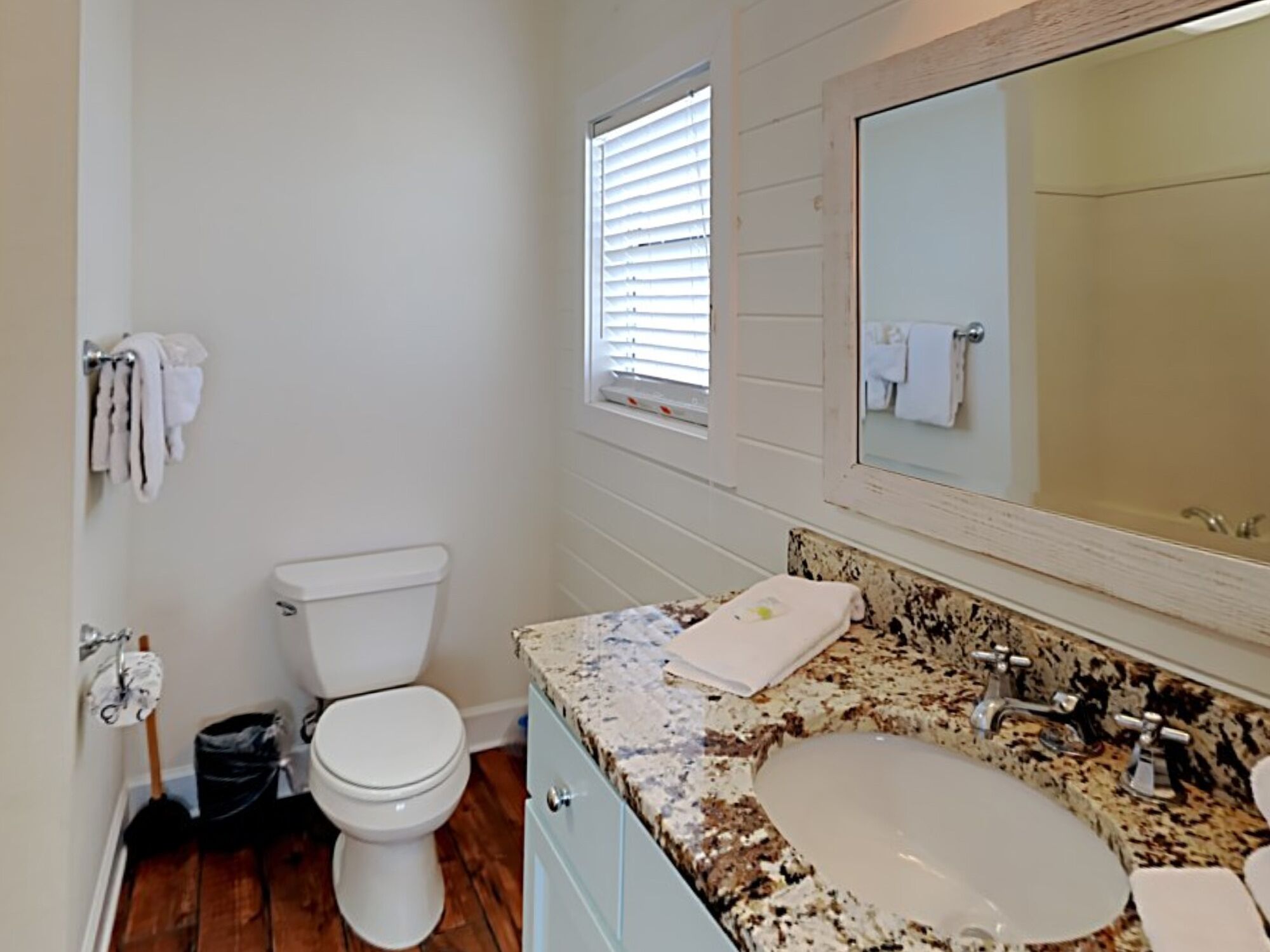 Un baño con inodoro blanco, lavabo con encimera de granito y espejo sobre el lavabo.