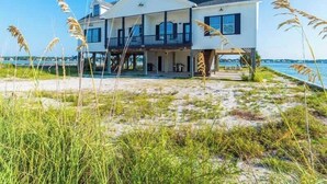 A two-story beachfront house with a balcony, a covered porch, and a sandy beach in the foreground. - Muskoka by Southern Vacation Rentals (Gulf Shores)
