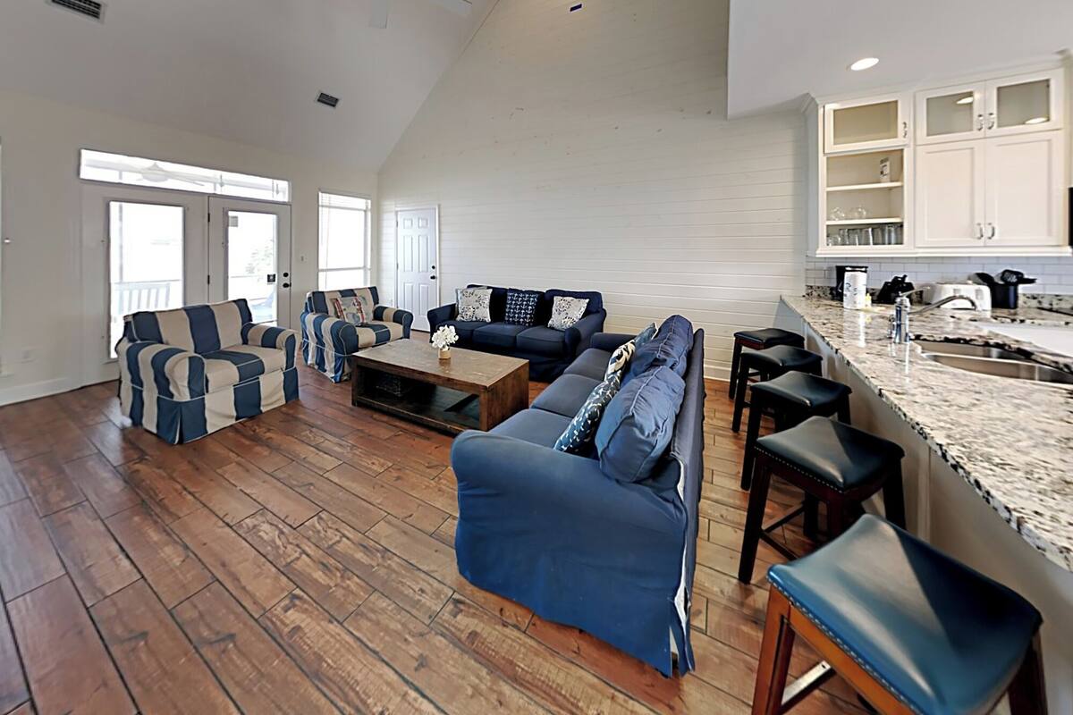 A spacious living area with a high ceiling, hardwood flooring, and a kitchen with white cabinets and a granite countertop.