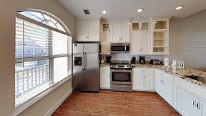 A kitchen with white cabinets, a stainless steel refrigerator, a microwave, an oven, and a granite countertop. - Muskoka by Southern Vacation Rentals (Gulf Shores)
