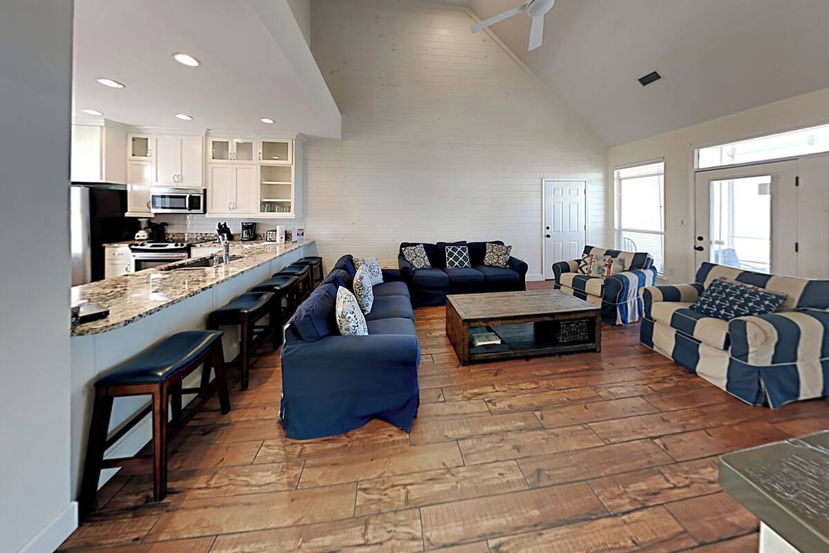 A spacious living area with a kitchen, wooden flooring, and a ceiling fan.