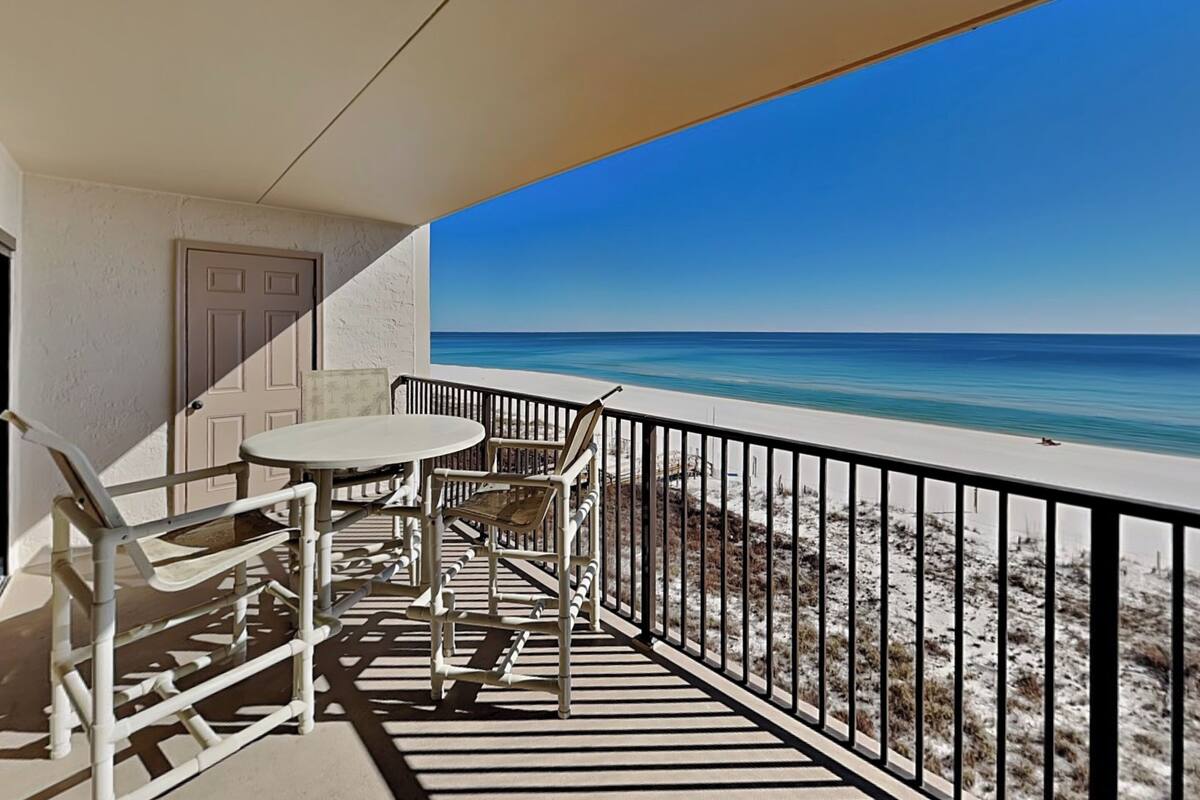 A balcony with a table and chairs, a door, and a view of the beach.