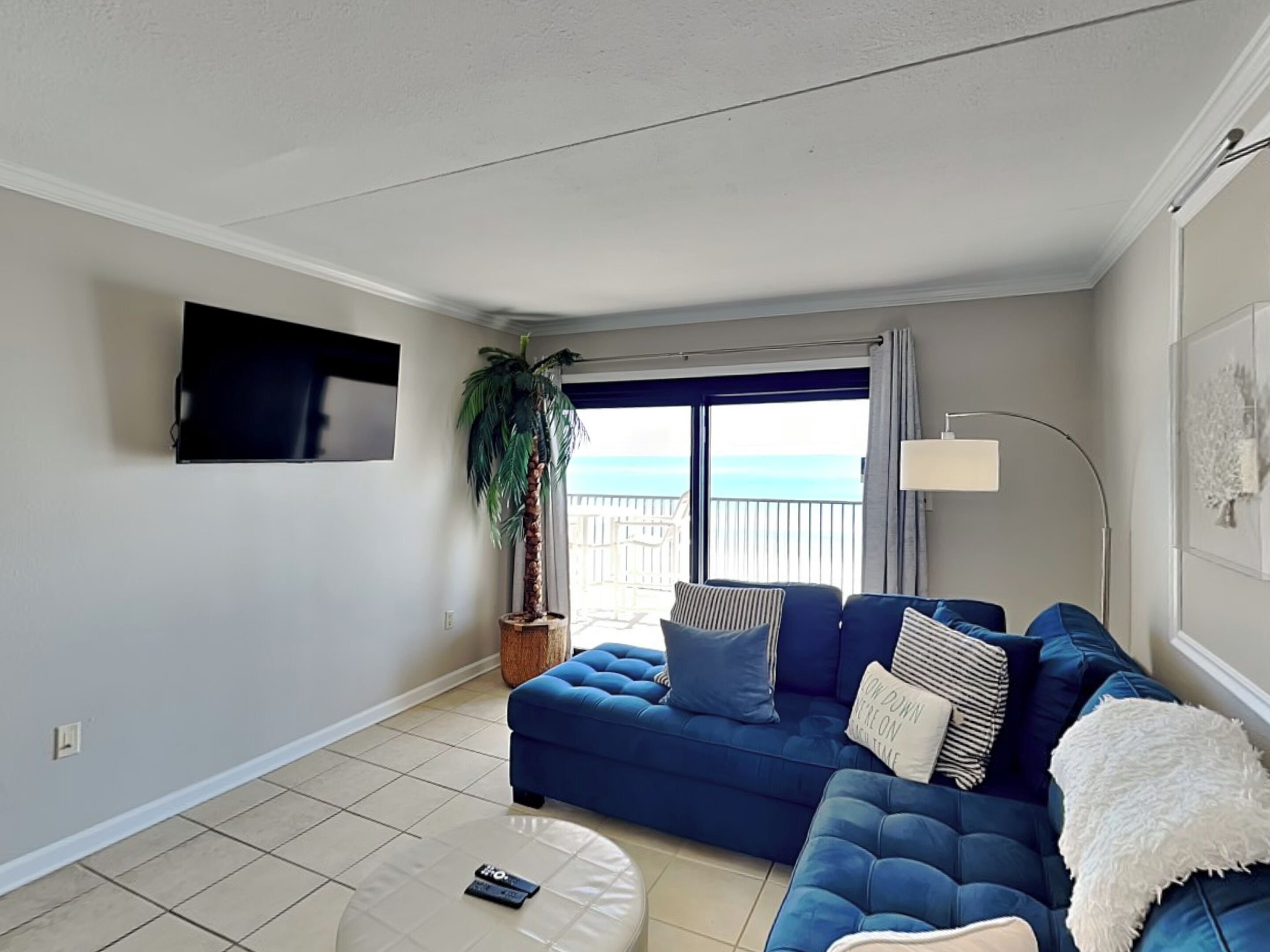 Ein Wohnzimmer mit einem blauen Sofa, einer Topfpflanze und Meerblick durch eine Schiebetür.
