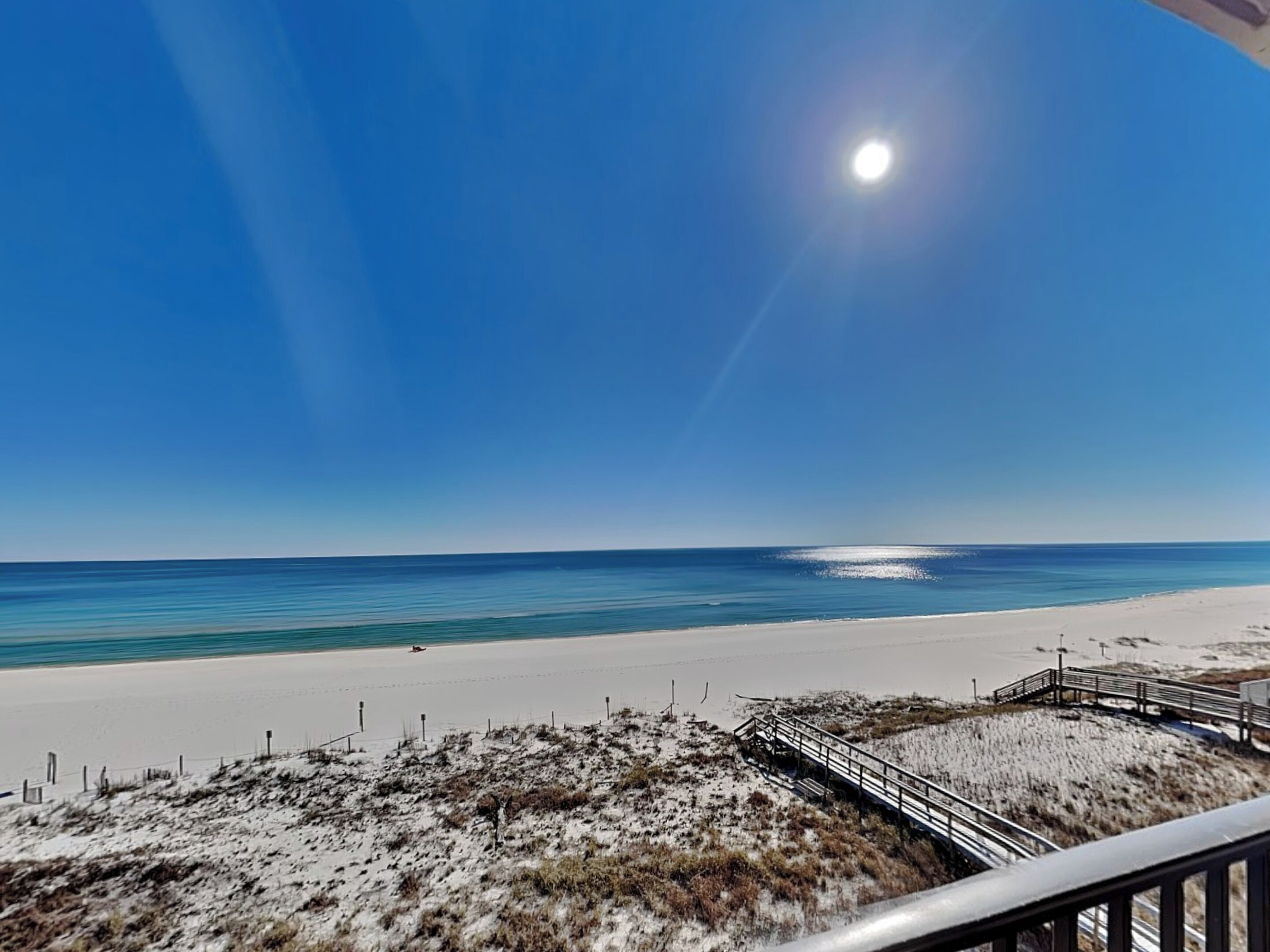Une plage avec un ciel dégagé, un rivage sablonneux et une promenade en bois qui mène à l’eau.